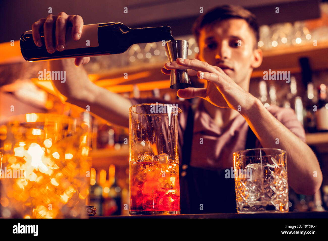 Dark-haired bartender adding some alcohol to the cocktail Stock Photo