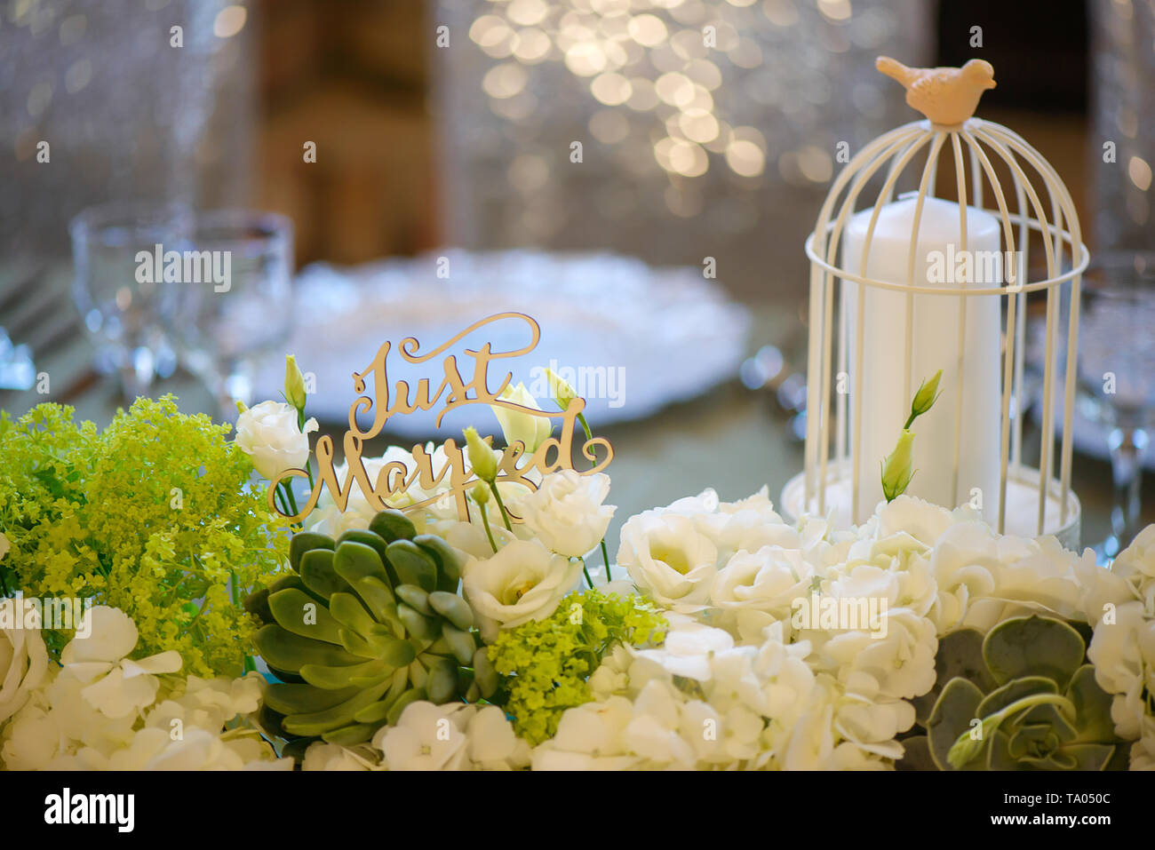 Wedding romantic decor for bride and groom dinner table with white vintage decorative bird cage holding a white candle and mixed flowers bouquet Stock Photo