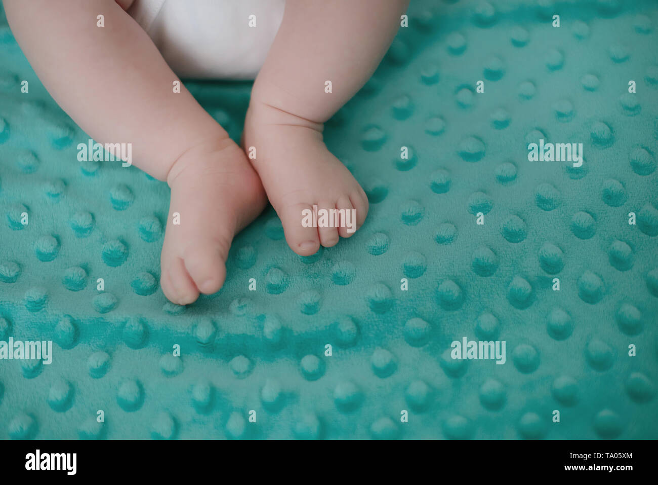Tiny newborn baby feet resting on a green soft blanket. Cropped shot with healthy Caucasian infant feet and copy space, concept for new life Stock Photo