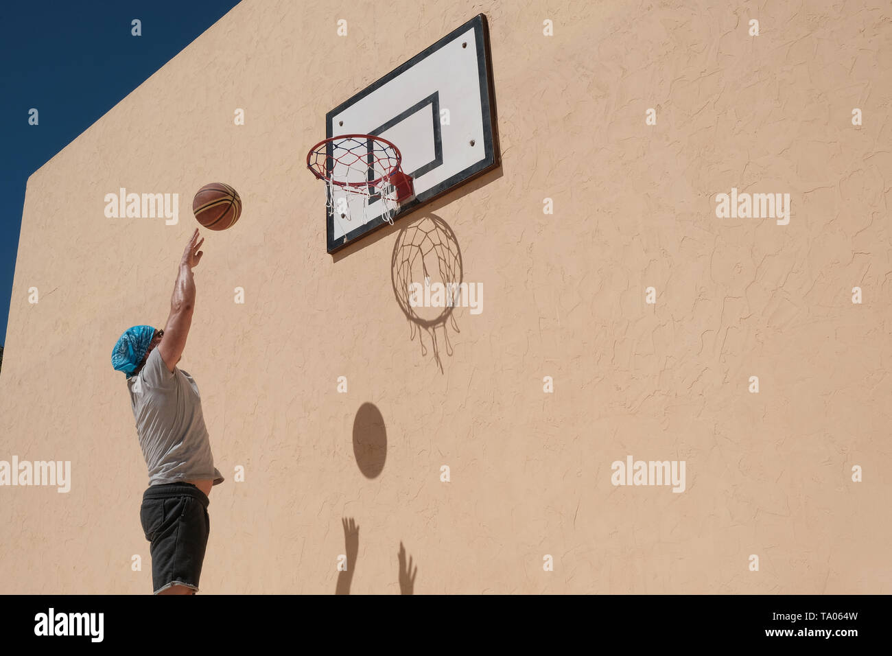 one man playing basketball. The ball and the net create shadows on the yellow wall. Stock Photo