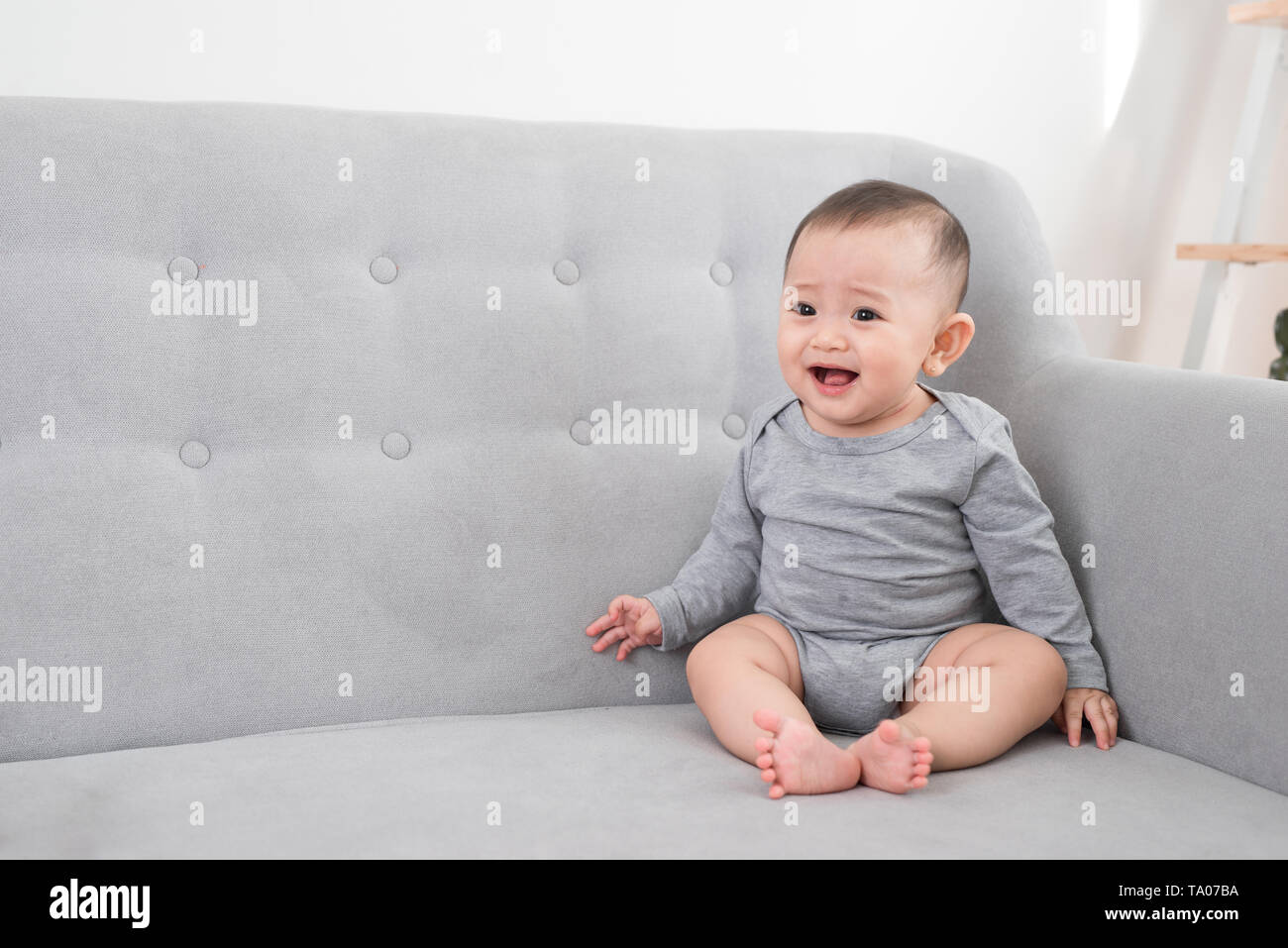 childhood, babyhood and people concept - happy little baby girl sitting on sofa at home Stock Photo