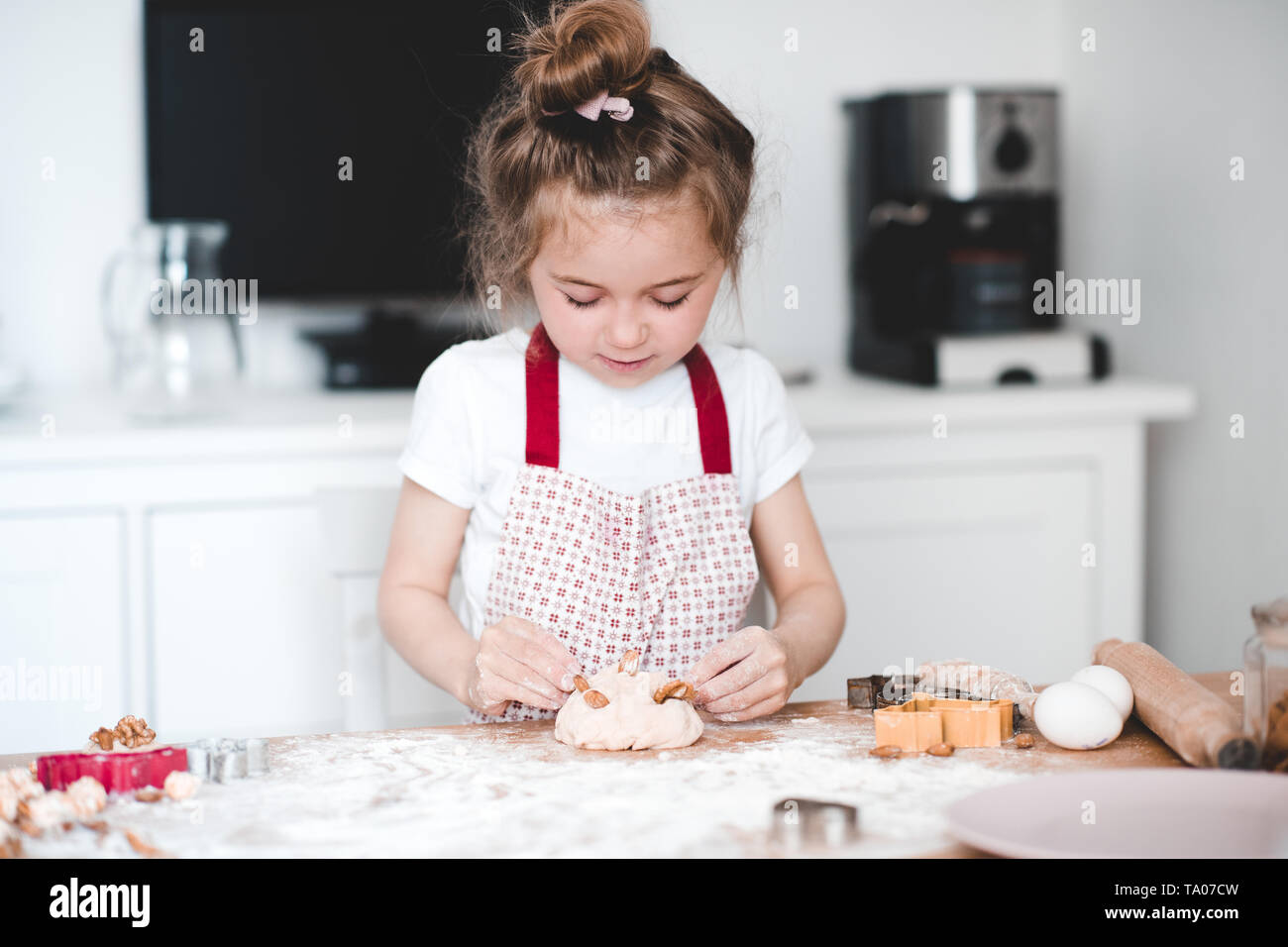 Pretty kid girl 3-4 year old making cake with almond cooking at kitchen closeup. Childhood. Stock Photo