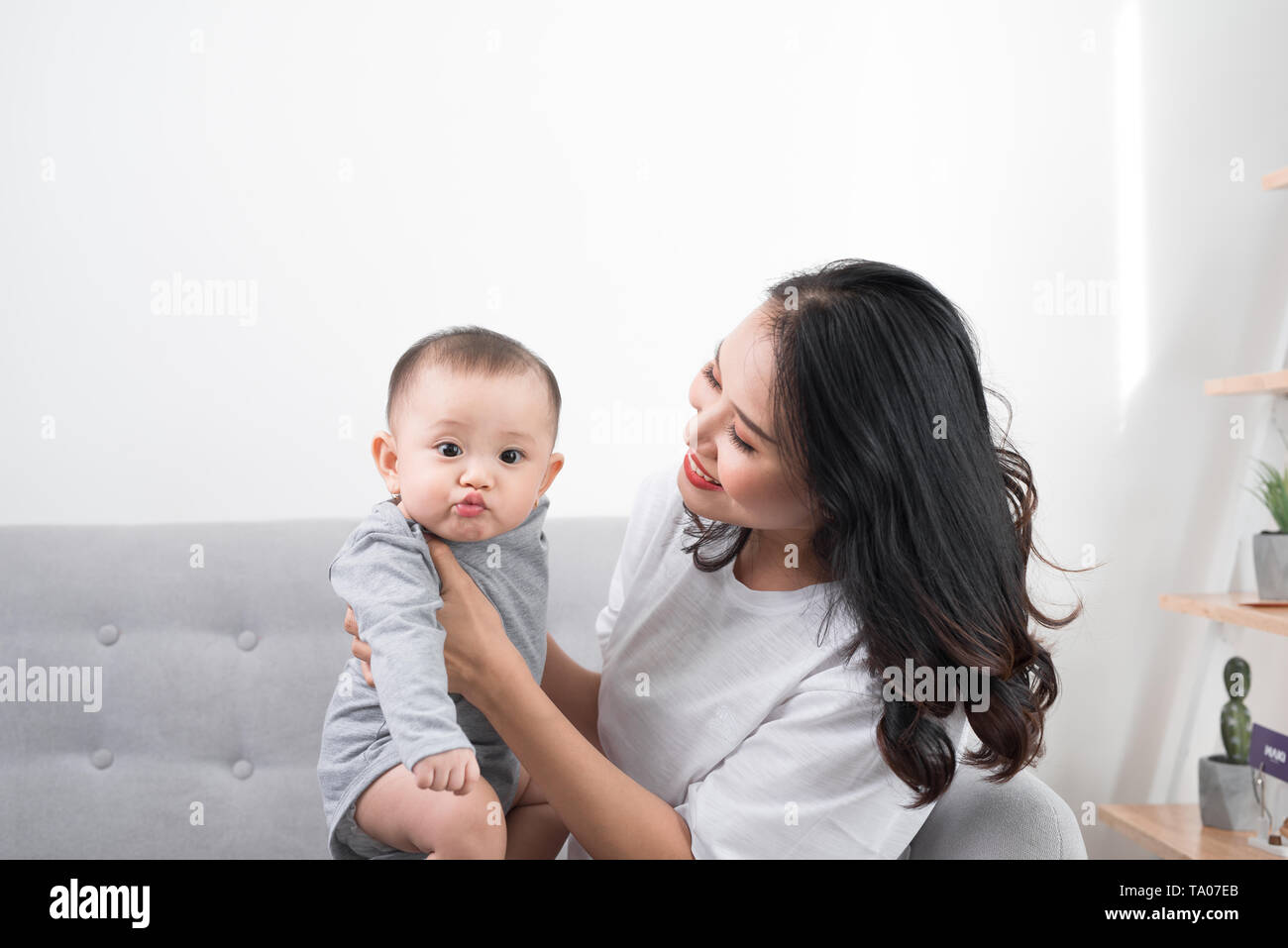 Young mother with her one years old little son dressed in pajamas are relaxing and playing in the living room at the weekend together, lazy morning, w Stock Photo