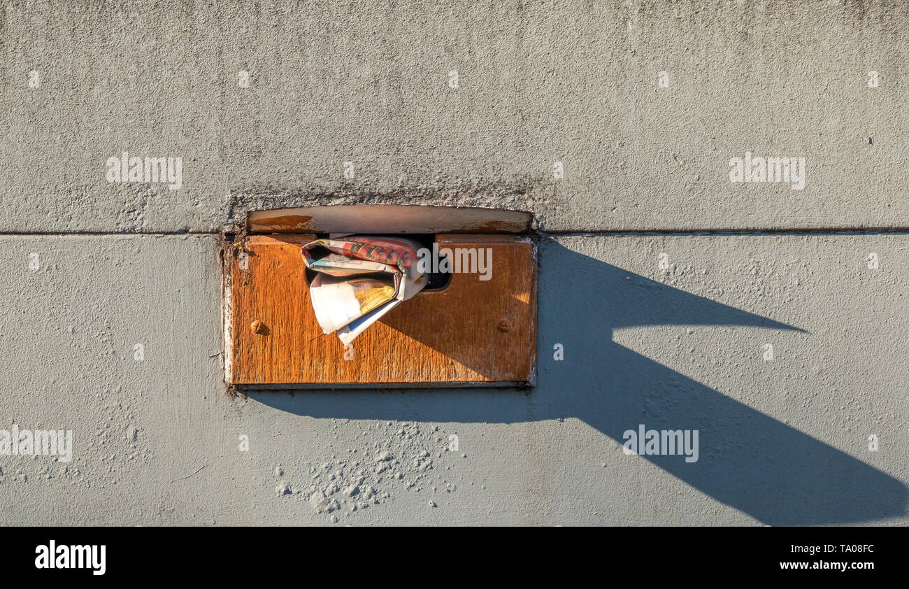 Hand delivered mail sticking out from a weathered domestic mailbox isolated on a dirty wall