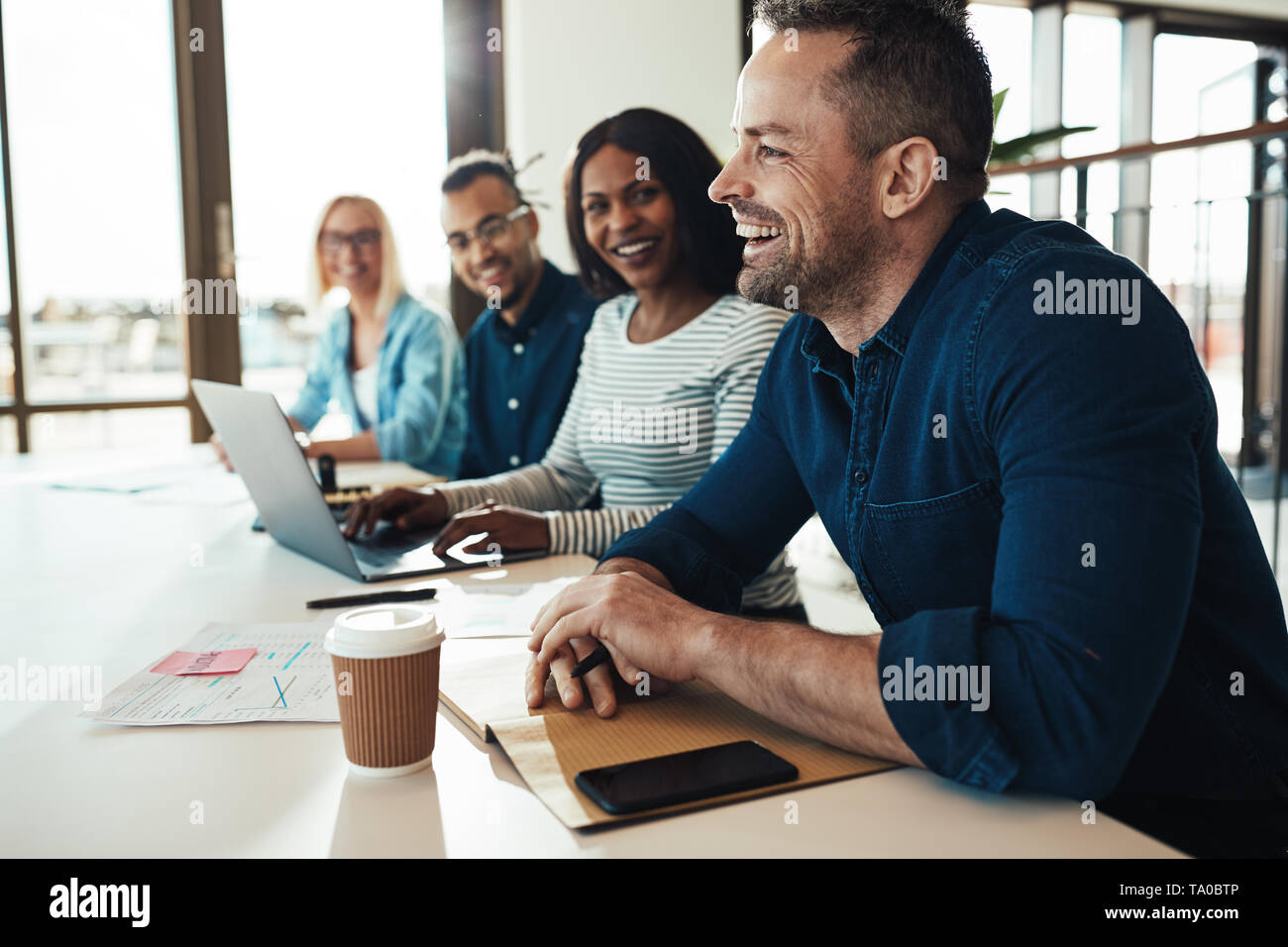 Mature businessman laughing while sitting with a diverse group of coworkers during a meeting in an office Stock Photo