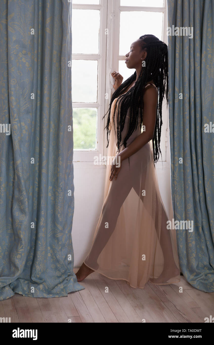 Beautiful woman in sheer nightgown looking out of a window with