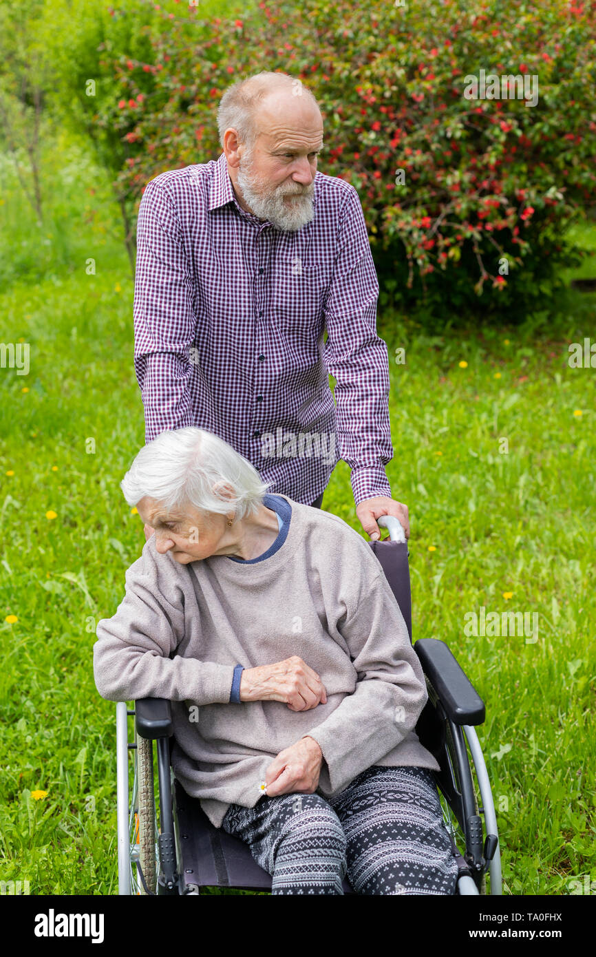 Old lady with severe dementia sitting in a wheelchair, spending time outdoor with carer Stock Photo