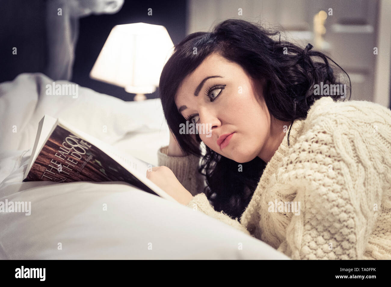 Young woman laying on a bed reading a book. Stock Photo