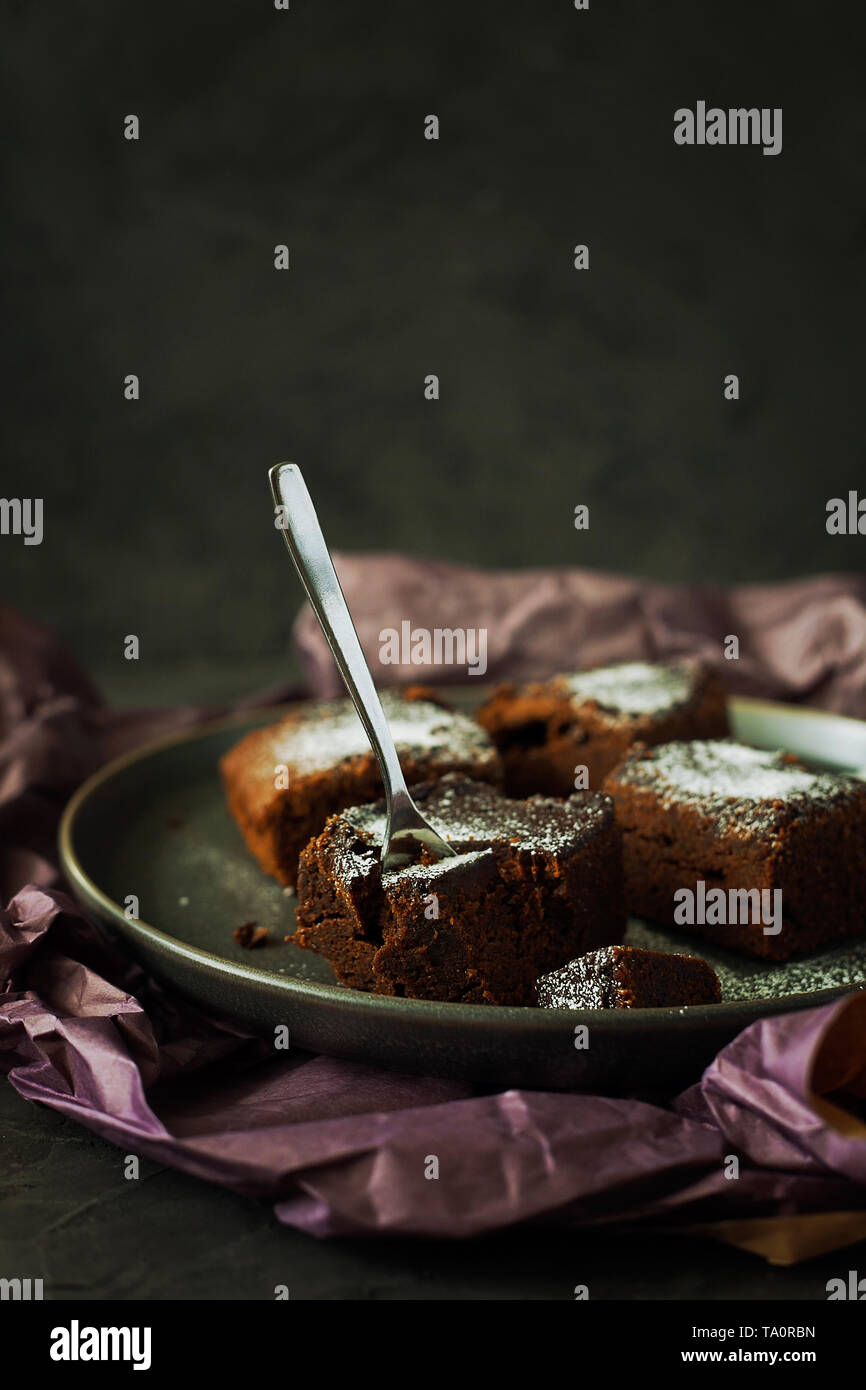 Piece of delicious vegan dairy-free dark chocolate brownies dessert or square moist sponge cakes cooked without eggs and decorated with powdered sugar Stock Photo
