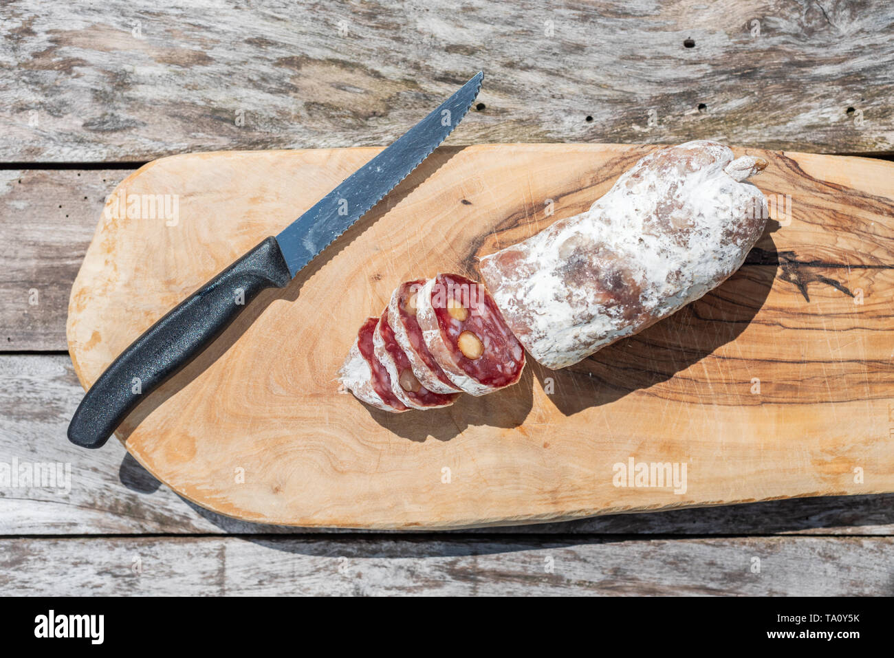 Dried sausage with nuts cut in slices and a knife close-up view on a wooden table Stock Photo