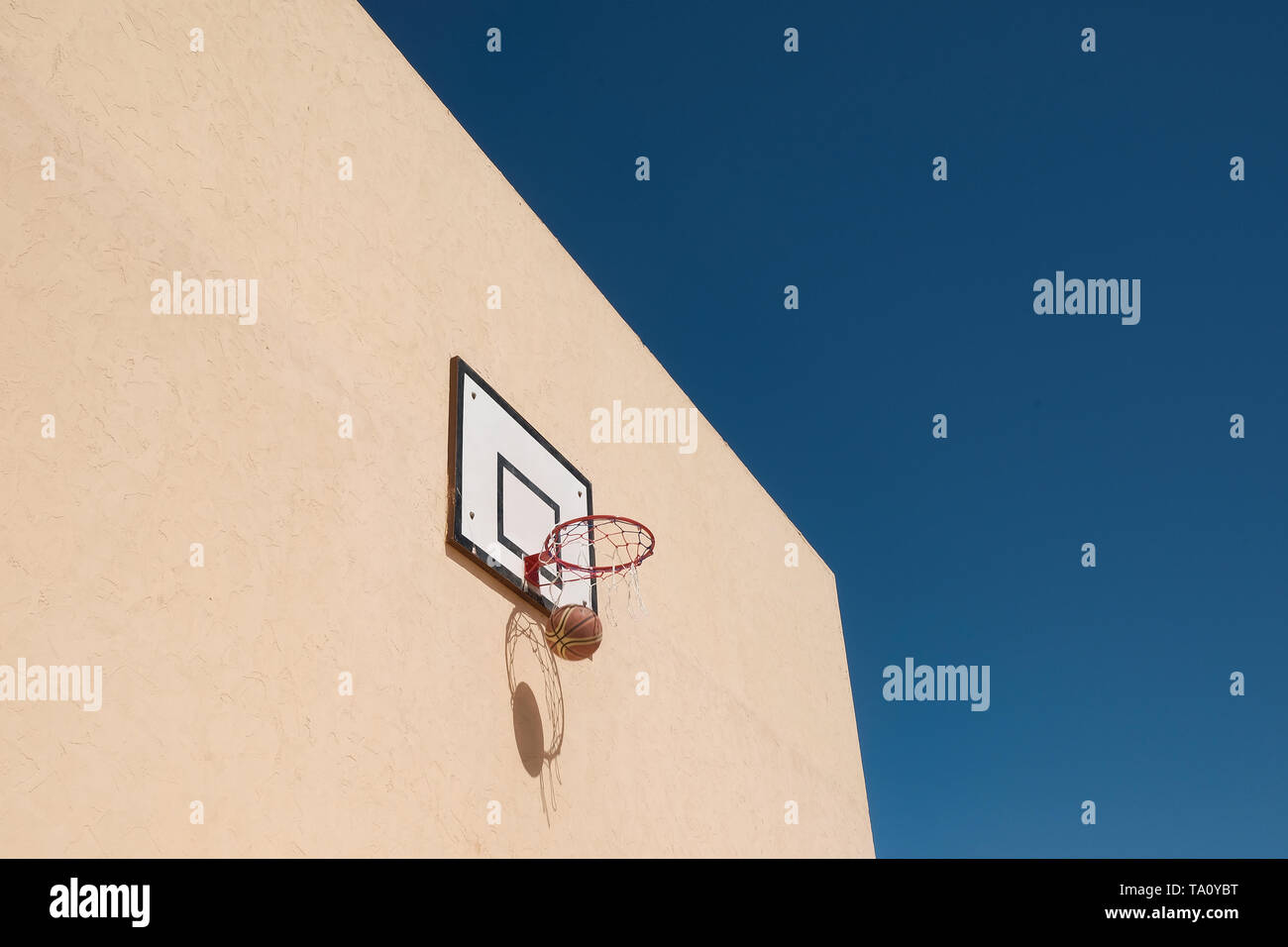 Basketball and basketball hoop create shadows on a yellow wall. Success