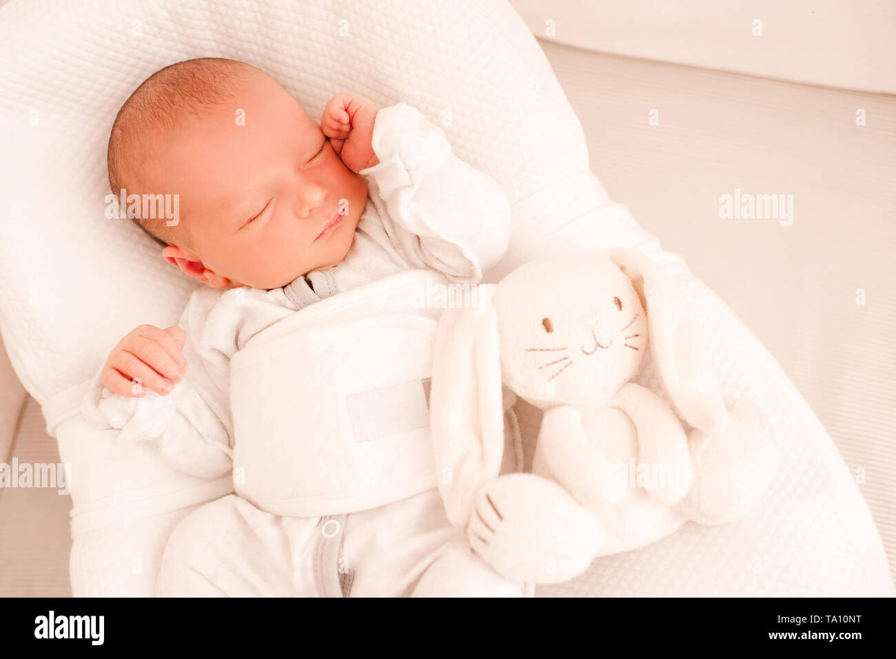 Smiling baby sleeping with toy in cocoon in bed closeup. Top view