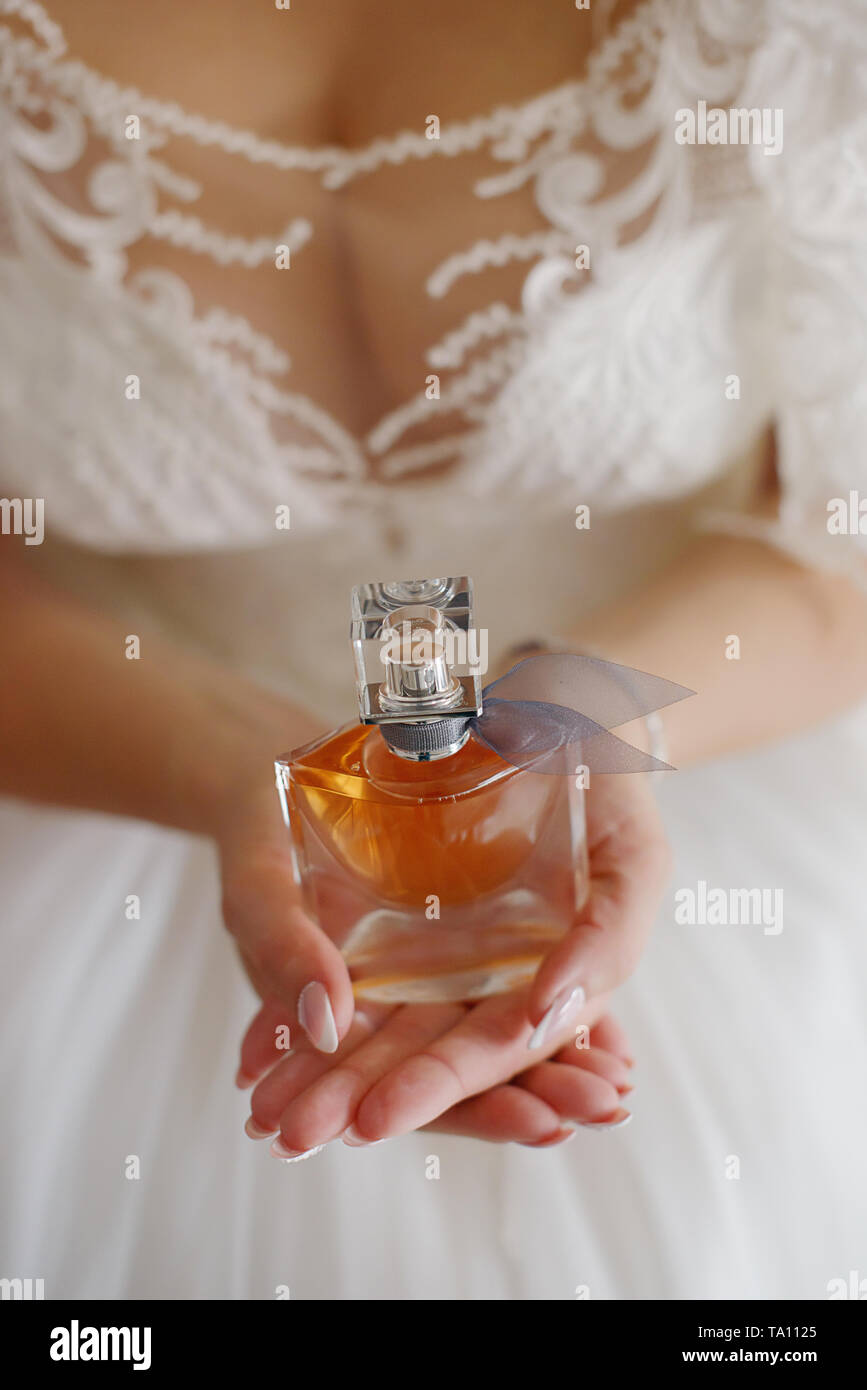 Vertical perspective of a young Caucasian bride wearing a white embellished lacy wedding dress with elegant manicure and holding a perfume bottle Stock Photo