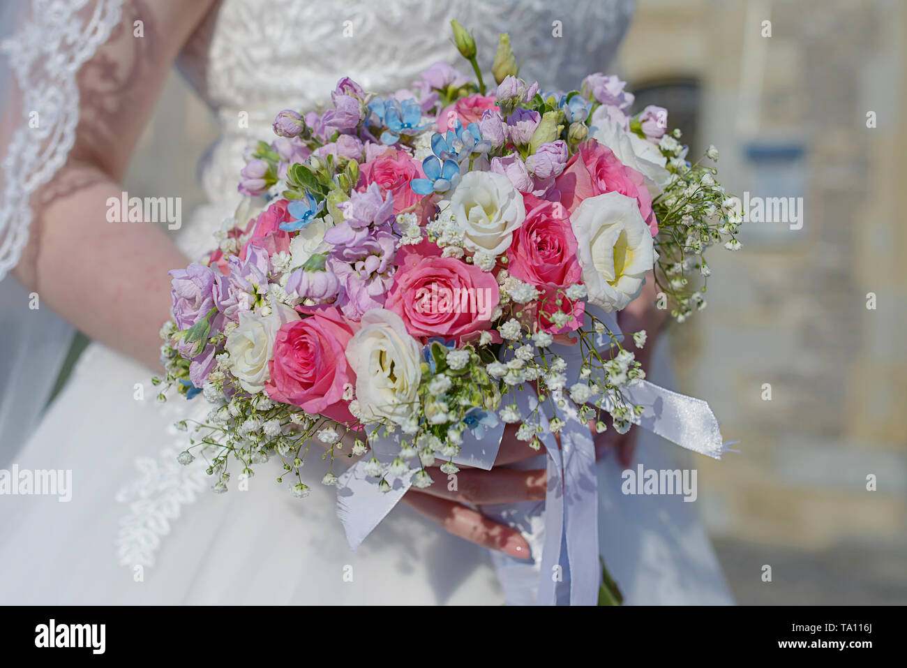 Classy young bride at the wedding ceremony with focus on the hand holding a floral arrangement, a round bouquet featuring pink and white roses Stock Photo