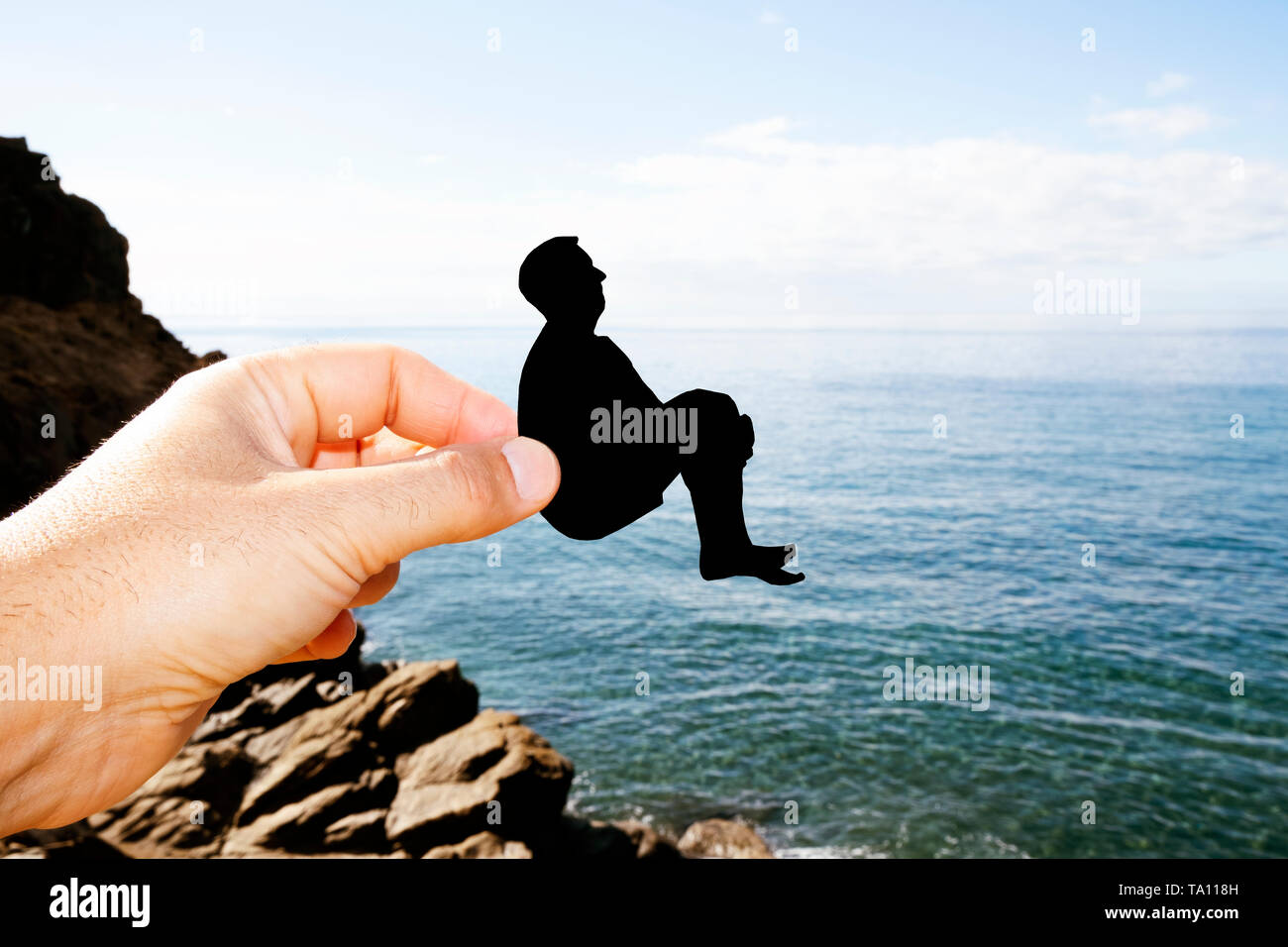 closeup of the hand of a man with a black paper cutout in the shape of a man about to throw himself into the ocean Stock Photo