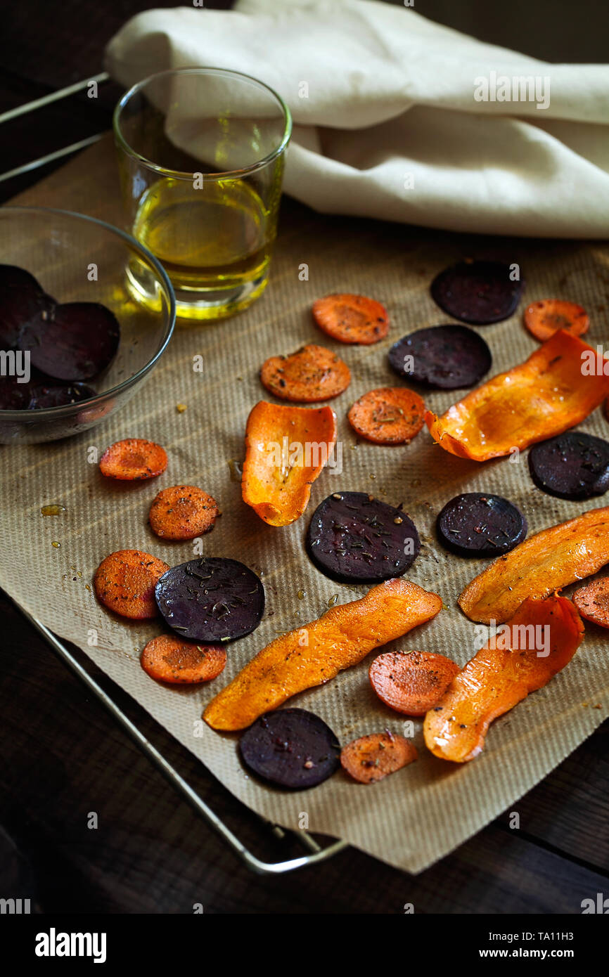 Preparing healthy beetroot and carrot chips with sea salt on baking paper.Thin slices of vegetables seasoned with spices and olive oil Stock Photo