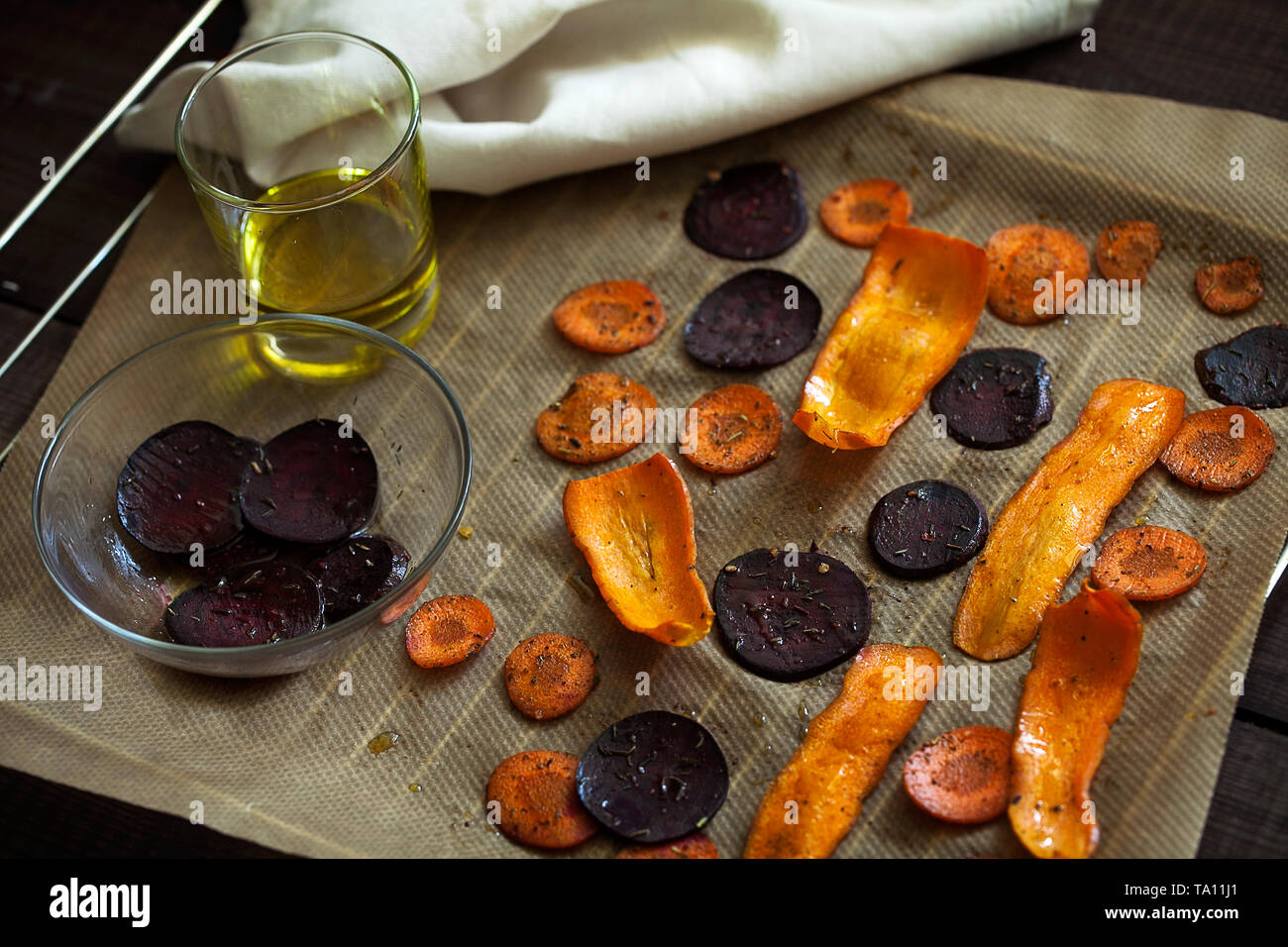 Preparing healthy beetroot and carrot chips with sea salt on baking paper.Thin slices of vegetables seasoned with spices and olive oil Stock Photo