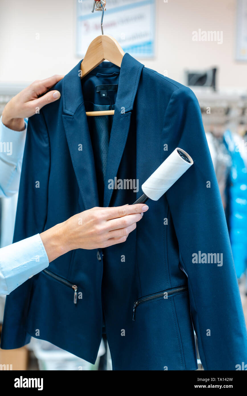 Woman in dry cleaning store is using lint roller to clean a jacket Stock Photo