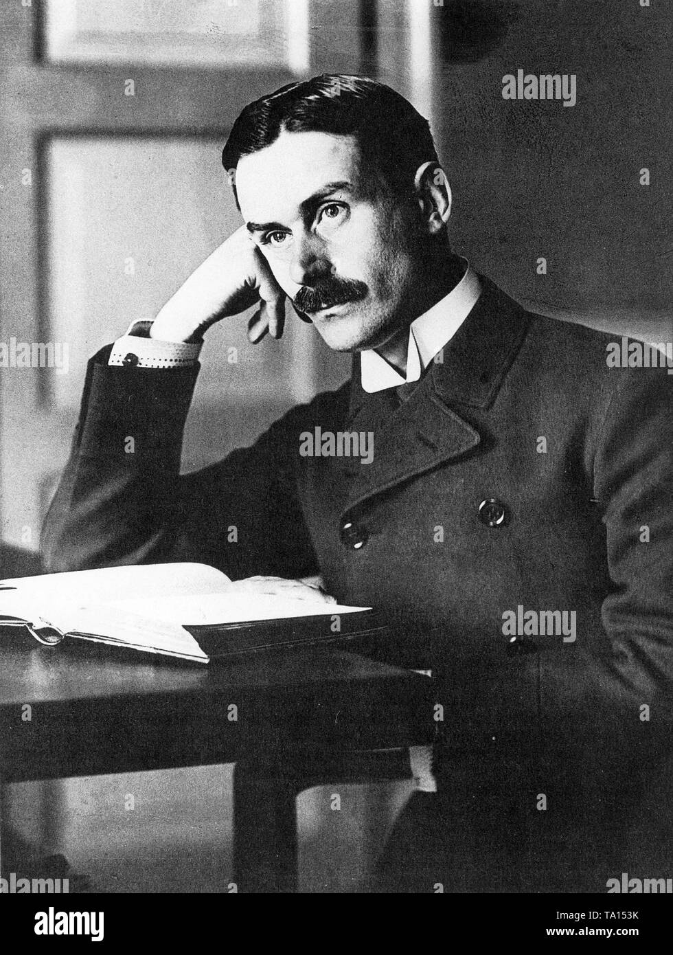 Pensive portrait of Thomas Mann sitting at a table with an open book. Stock Photo