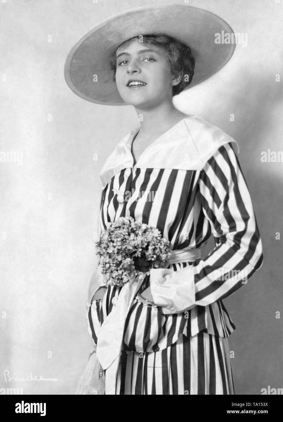 Mady Christians, a German actress, in a waisted striped jacket dress with front pockets and flowers in the waistband. Stock Photo