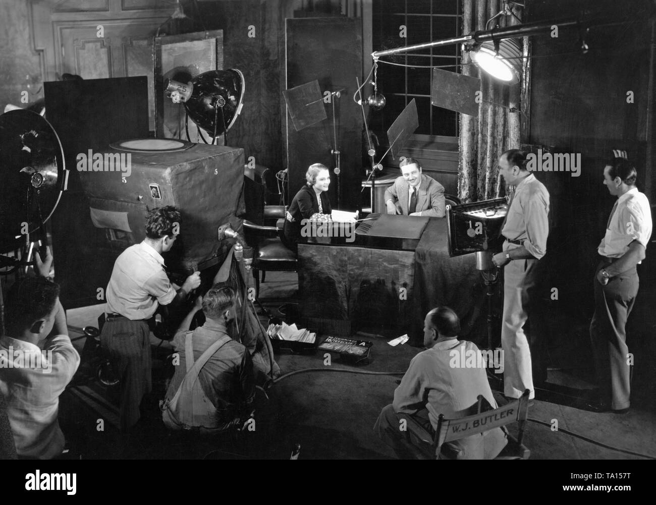 This photo was taken during the shooting of the crime film "Attorney for the Defense", directed by Irving Cummings, at Columbia Studios in Hollywood. In the picture: Constance Cummings (sitting) and Edmund Lowe, standing beside: Irving Cummings. This movie was filmed with the best film technology of the time, the camera is hidden in a special box, the new microphone helps the actor to speak naturally. Stock Photo