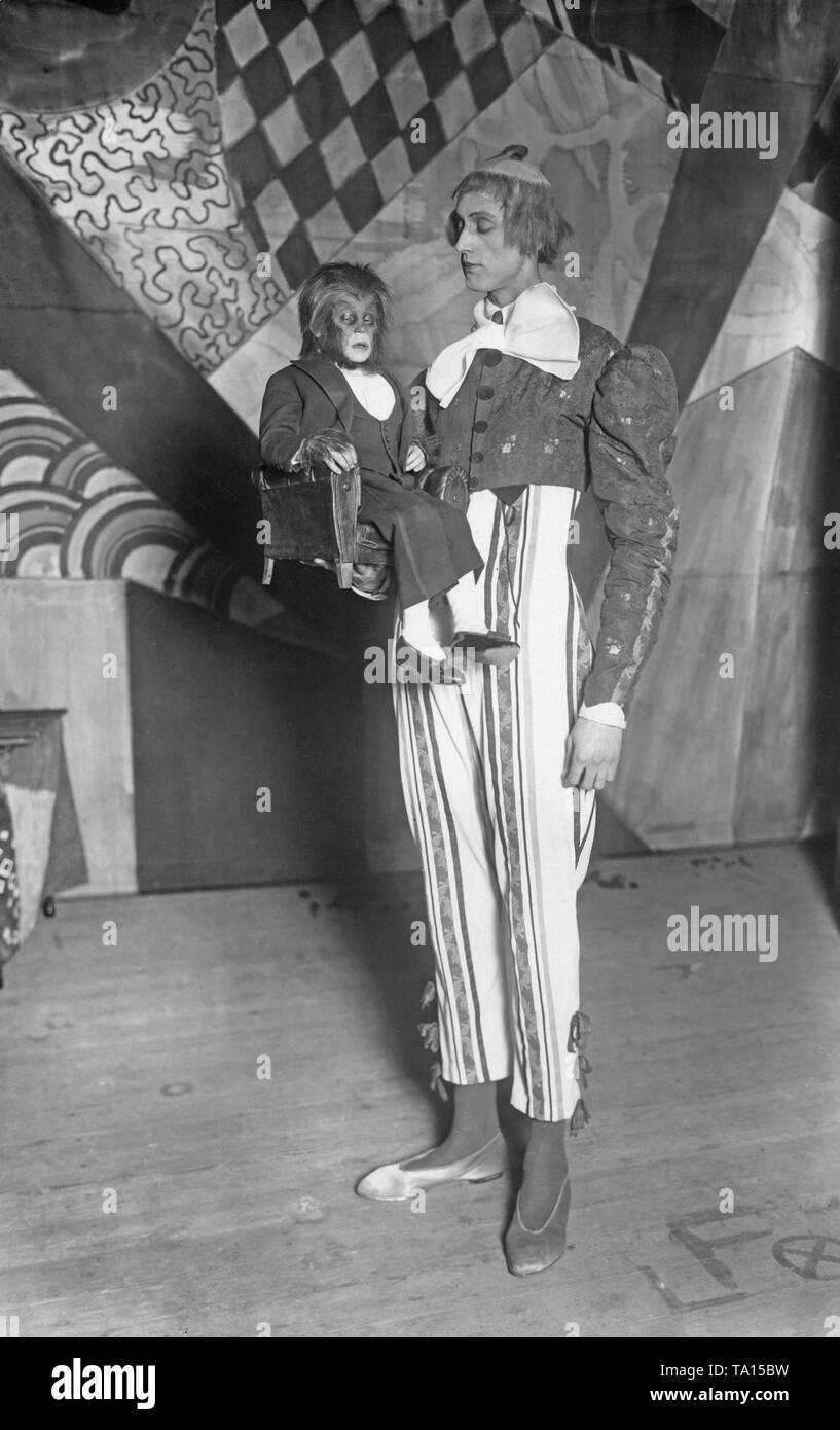 A man of small stature, dressed as a monkey, is held by a tall man in clown costume (Undated shot). Stock Photo