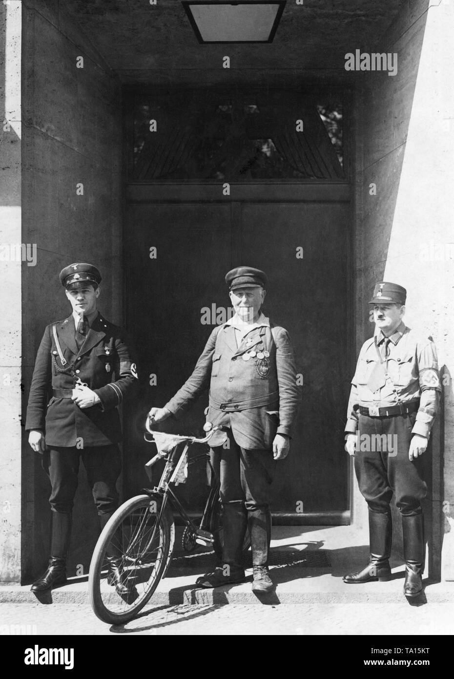 The oldest active cyclist, the retired railway official Heinrich Werner from Heidenburg, 84 years old, is photographed in front of the entrance to the Berlin Radio House. Characteristic of this time, shortly after Hitler's takeover, two SS guards stand before the entrance. Stock Photo