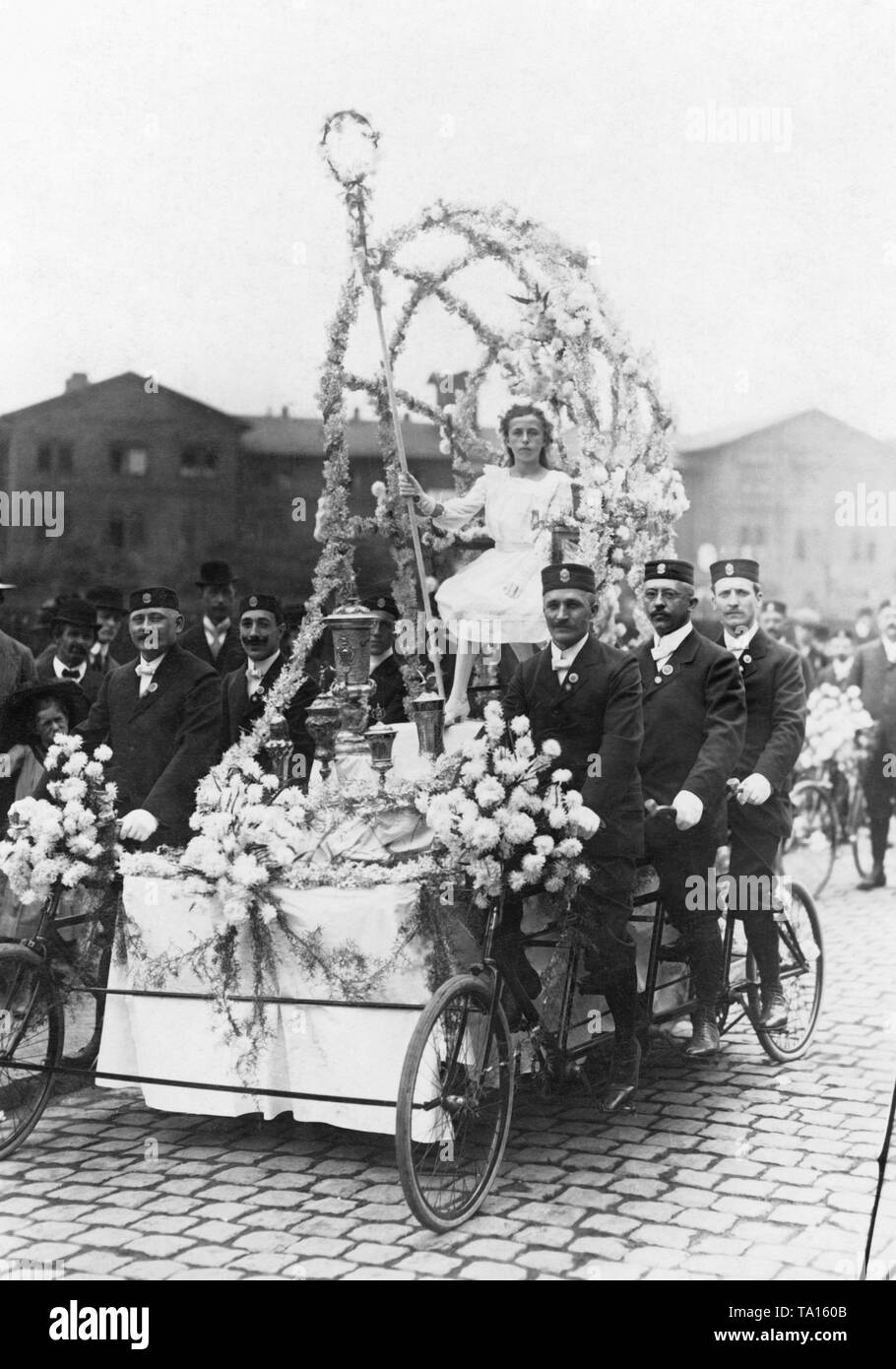 Flower-bedecked group from the pageant at the 25th Bundestag des Deutschen Radfahrerbundes (Day of the German Cycling Federation). In the middle the 'Lady of Honor'. The men drive a wheel of the brand Bessier. Stock Photo