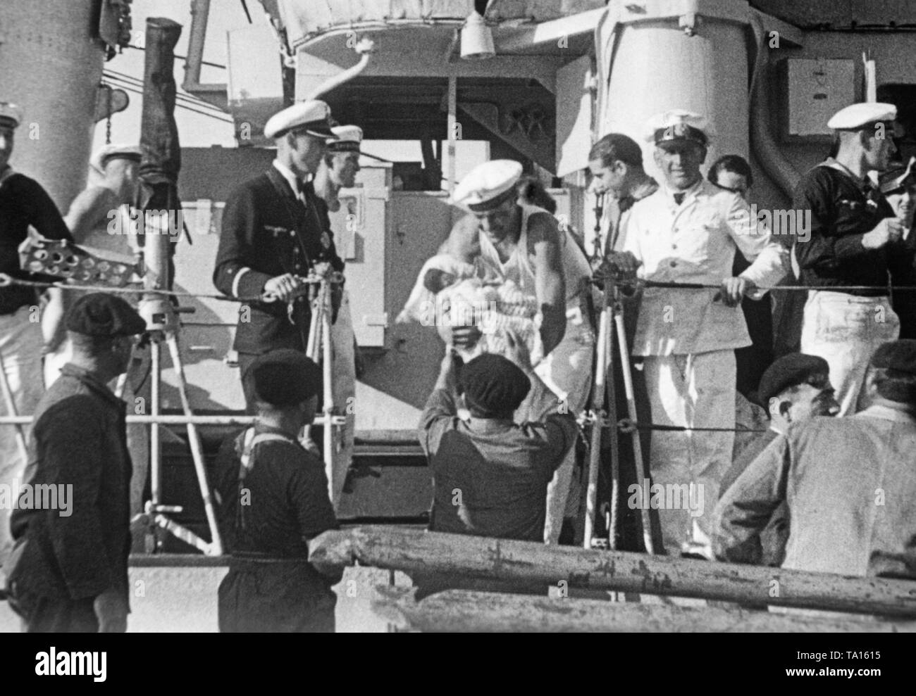 The German destroyers 'Jaguar' and 'Wolf' bring Spanish refugees to the port of St. Jean de Luz, French Basque country, France, during the Spanish Civil War on September 18, 1936. In the photo, a German sailor, who is handing over a baby from the deck. German naval officers are standing around the man taking the baby. Stock Photo