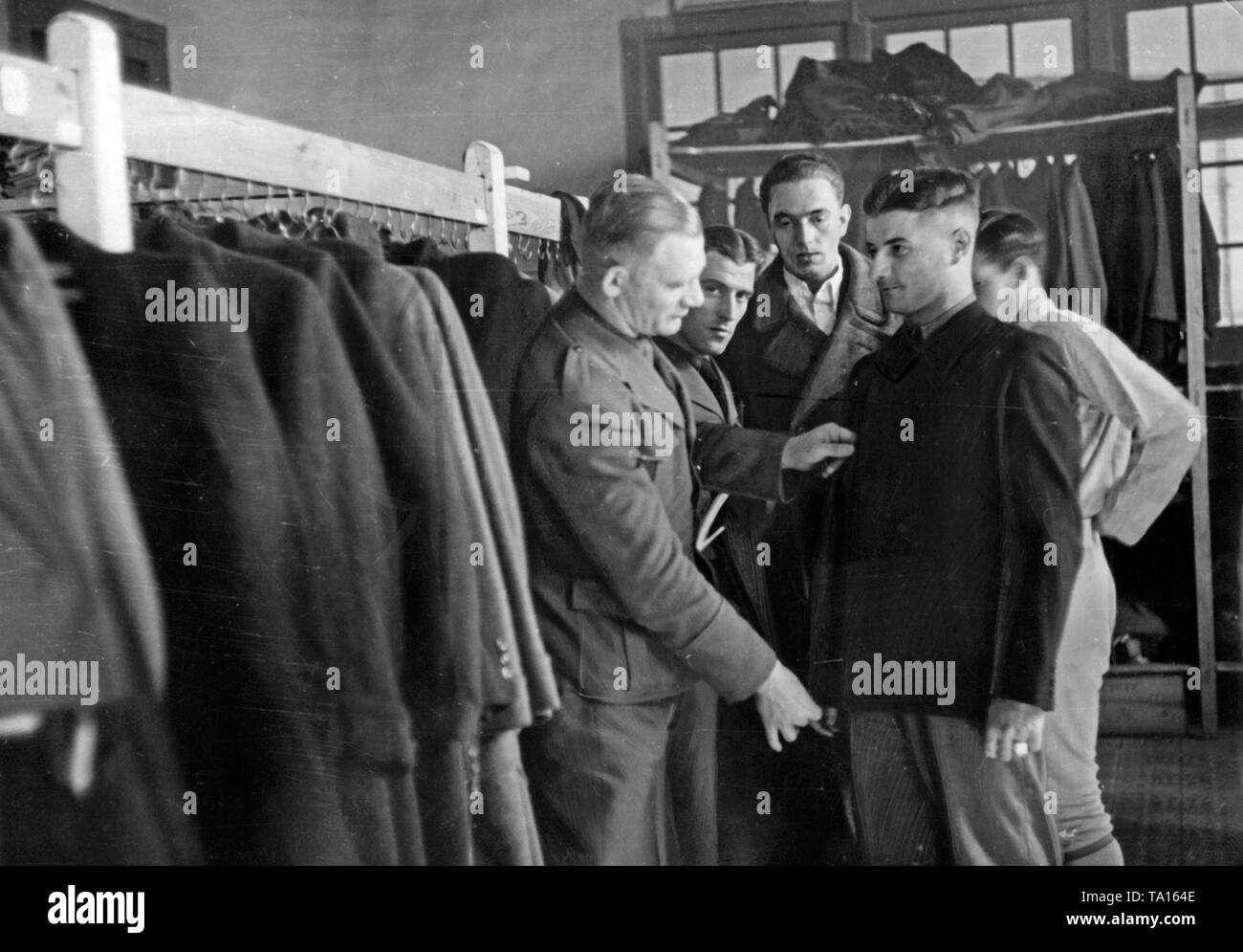 After the end of the Spanish Civil War (April 1939), soldiers of the Wehrmacht of the Condor legion were given civilian clothing by their comrades on their return to Germany in May 1939. A soldier is adjusting a jacket to a comrade. Behind, there are other soldiers standing. On the left, jackets and coats hanging on the clothes rail. Stock Photo