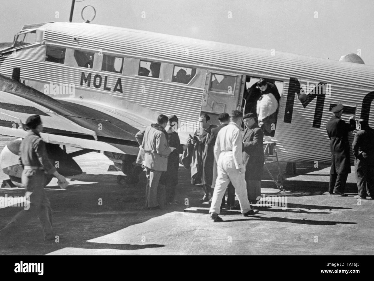 Photo of a German Junkers Ju 52 of the Spanish airline Iberia 1939 at the airport of Salamanca, Castile and Leon, Spain, through the windows of the new terminal. Soldiers and civilians are getting off the aircraft. The machine is named 'Mola', after general Emilio Mola Vidal (died 1937), one of the leaders of the uprising of General Francisco Franco. During the Civil War, the Deutsche Lufthansa and the Iberia (founded in 1927) carried out scheduled flights mostly with German pilots in the Spanish national zone from 1937. The aircraft were provided by the Deutsche Lufthansa AG. Stock Photo