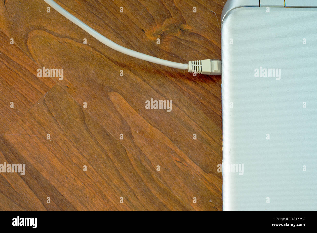 Closed laptop connected to ethernet grey cable on brown wooden floor ...