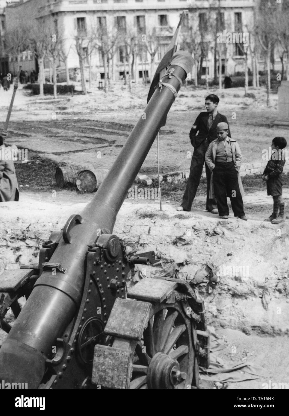 Photo of a Republican artillery gun after the entry of the Spanish national faction into the Spanish capital in the spring of 1939. The barrel is decorated with the Spanish Bandera, the national flag. Behind, there are children. Stock Photo