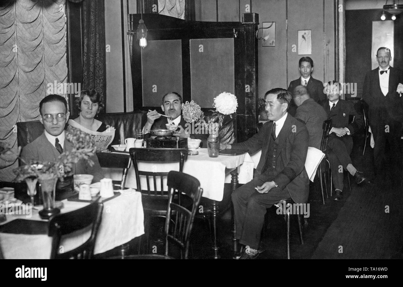A group of Japanese people sitting in a Berlin restaurant. Some of them  wear black armbands on the occasion of the death of the Japanese Emperor,  who died on December 25, 1926