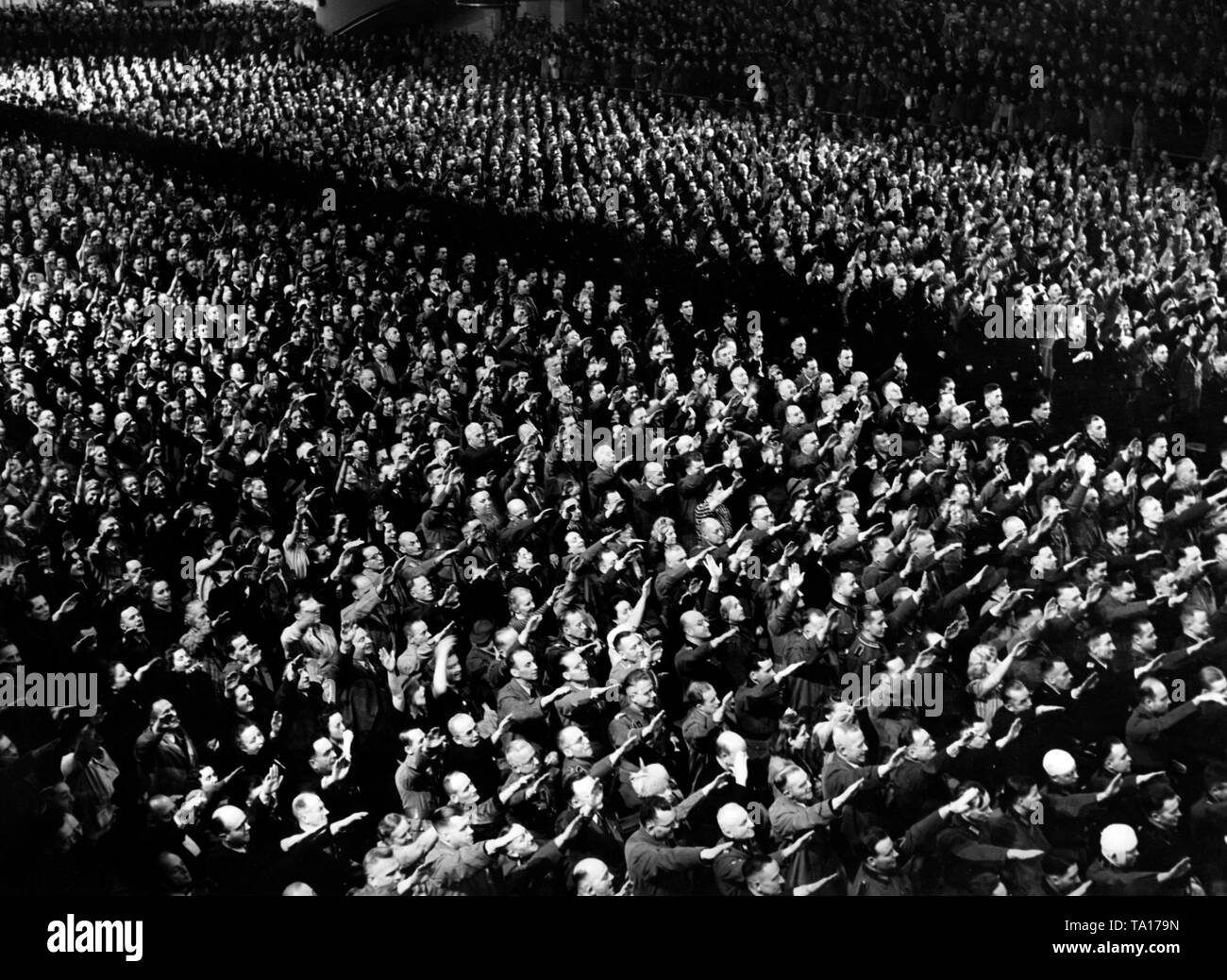 View of the audience at a mass rally on the occasion of the opening of the 3rd Kriegswinterhilfswerk in the Berlin Sportpalast, where Adolf Hitler gave a speech. The crowd has risen, and performs the Hitler salute. Stock Photo