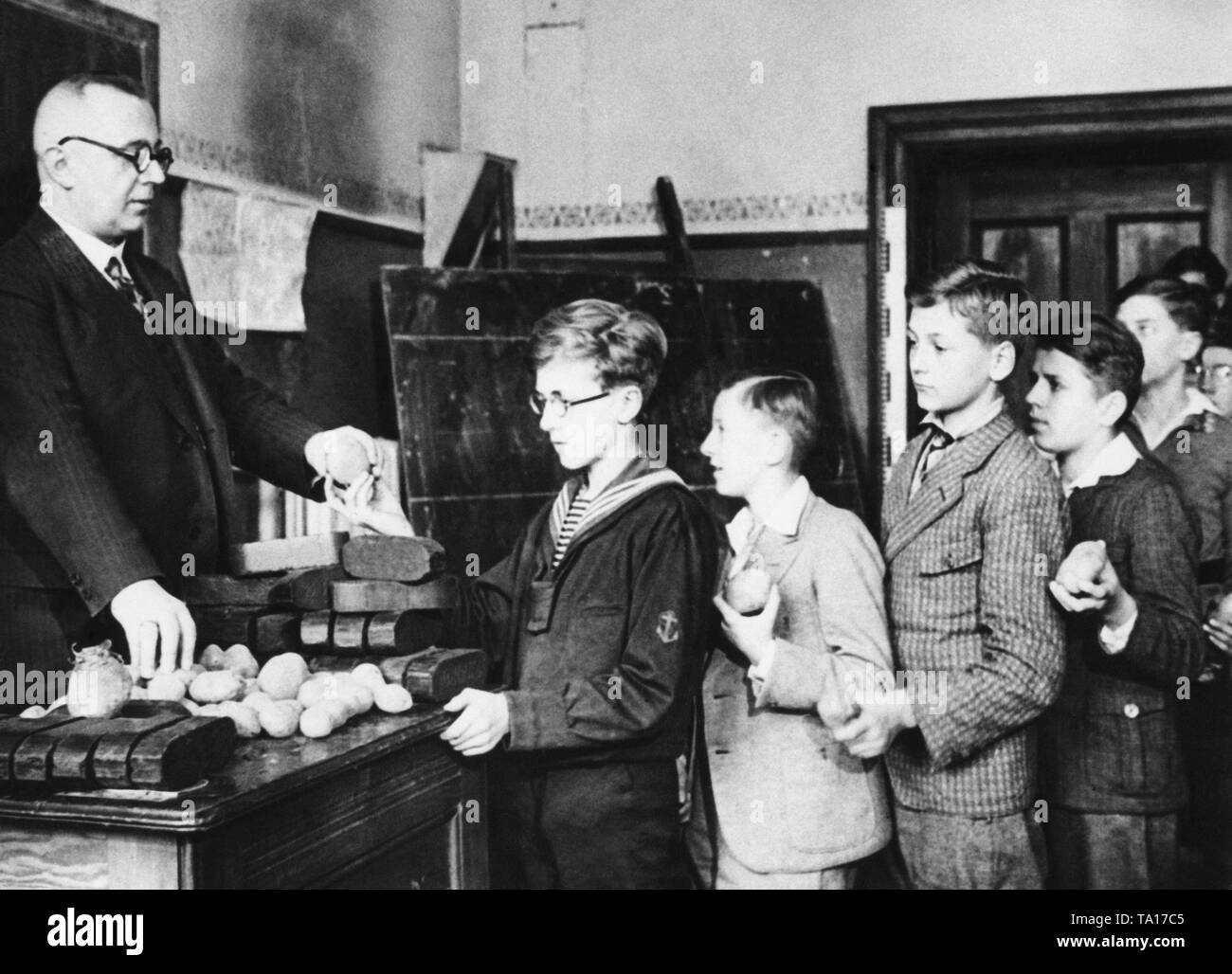 Students from the Kaiser Friedrich School in Berlin bring either a piece of pressed coal or a potato  in the school to help needy families. There the teacher collects these every morning before the class starts. The reason for the collection was the lasting mass unemployment and the plight of the affected families in the winter months of the economic crisis. Without date, probably in 1931. Stock Photo