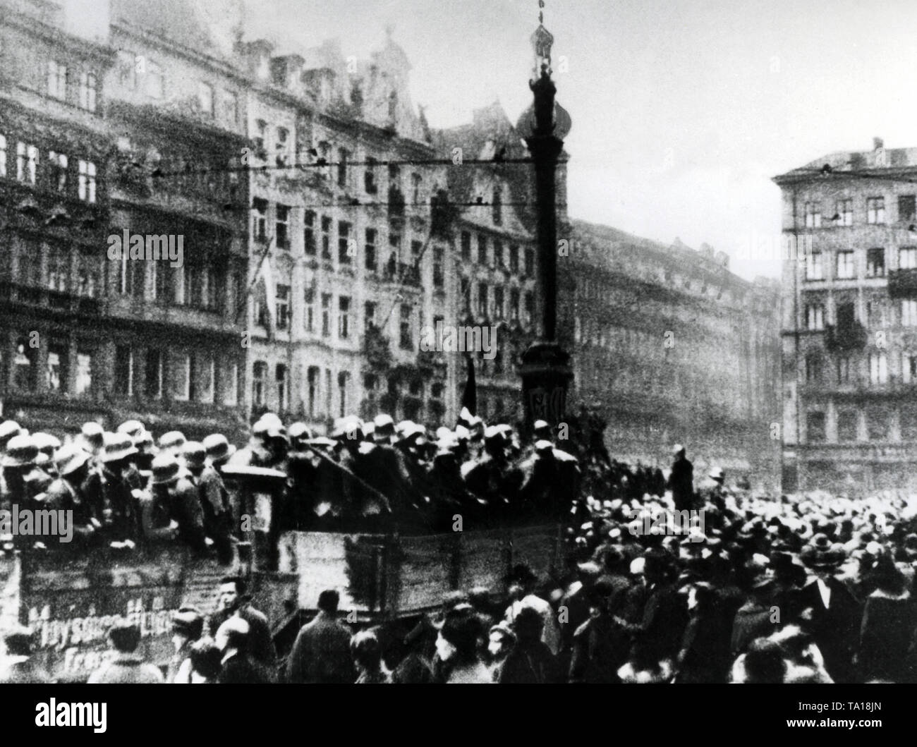 Members of a Freising SA unit stand on trucks at Marienplatz and listen to a speech of Julius Streicher (standing, below the Mariensaeule). The trucks and the speaker are surrounded by a crowd. Stock Photo