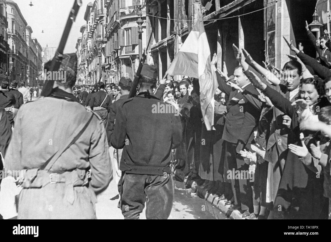 Photo of non-regular Spanish national units and city-dwellers during the invasion of Calle Marques de Larios, the main sales-street in Malaga on February 8, 1937. The fighters wear civilian clothes, military Gorillo cap, shoulder carabiners and Spanish national flags. The inhabitants of Malaga give the fascist salute on the right on the pavement. Stock Photo