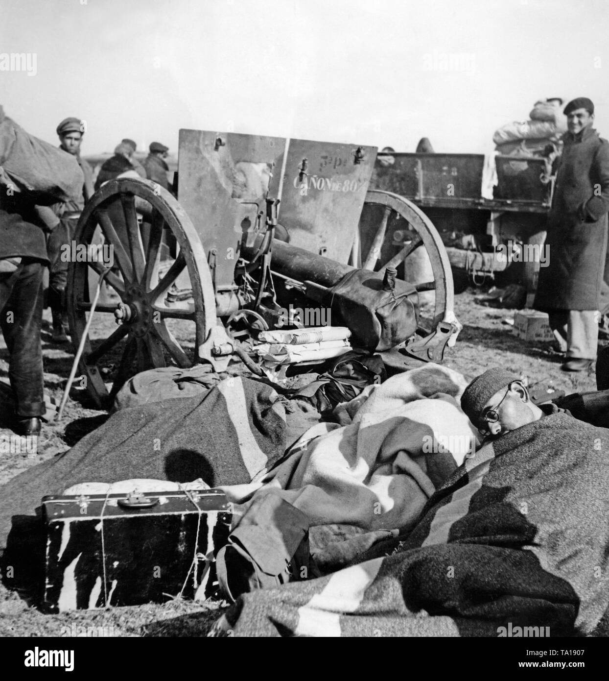 A group of Republican fighters camping behind the frontier. In the foreground a man is sleepign, behind are further refugees and guns. Stock Photo