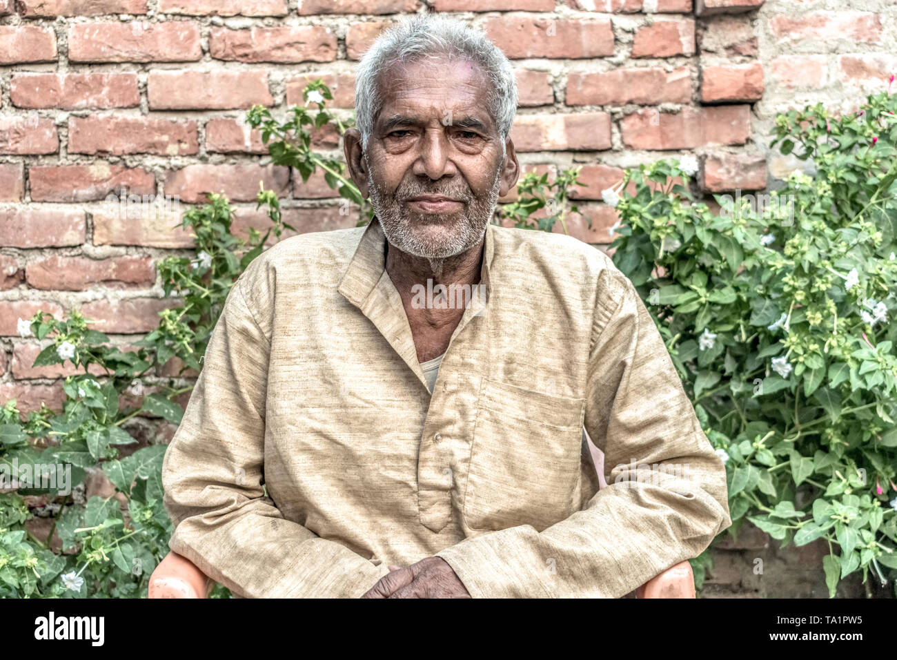 Portrait of Old aged Indian male in his 80s with white beard, wearing pale clothes, sitting relaxed in garden & leading satisfied post-retirement life Stock Photo