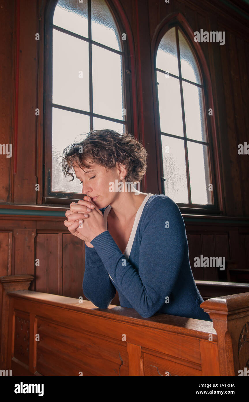 Young woman praying in the church with folded hands Stock Photo