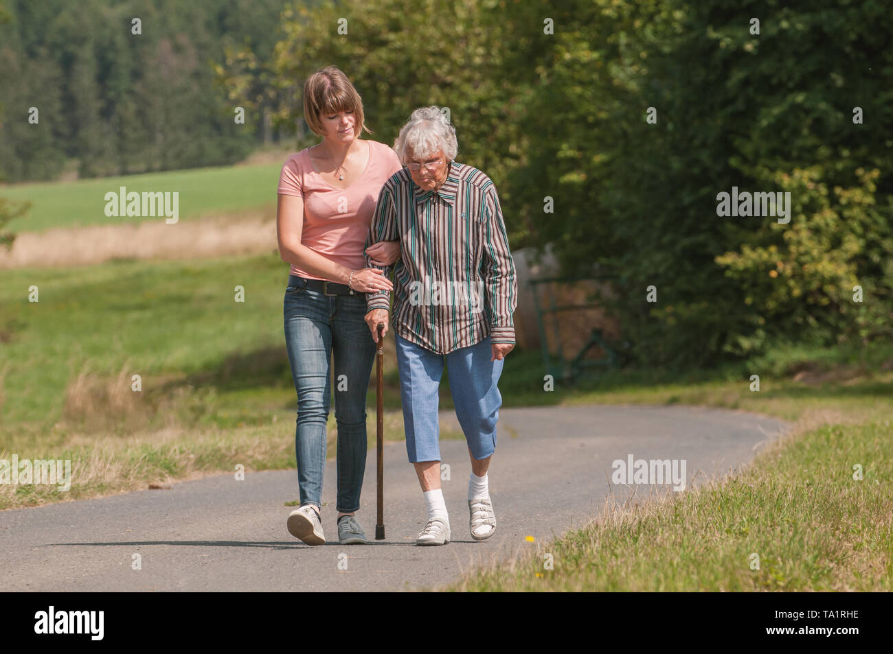 Young woman helping senior woman walking with stick Stock Photo