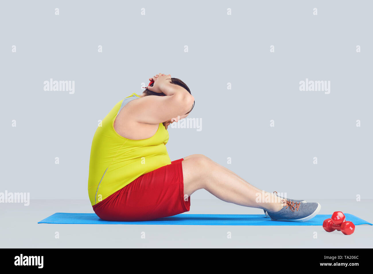 Fat funny man doing exercises on abs press on gray background Stock Photo