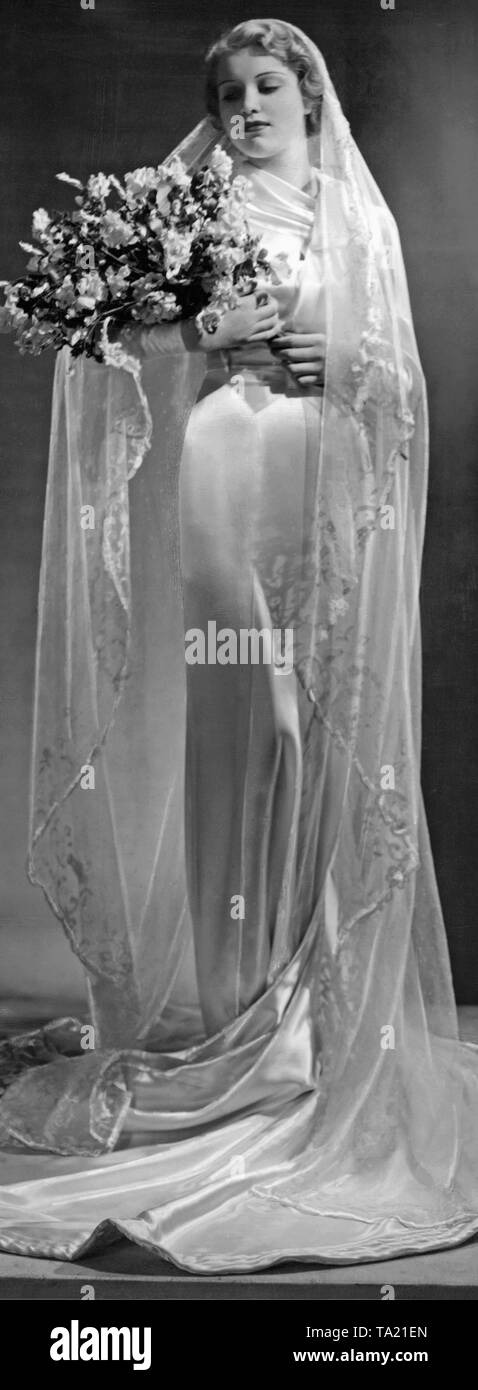 A mannequin presents a wedding dress with long train and patterned veil. Stock Photo