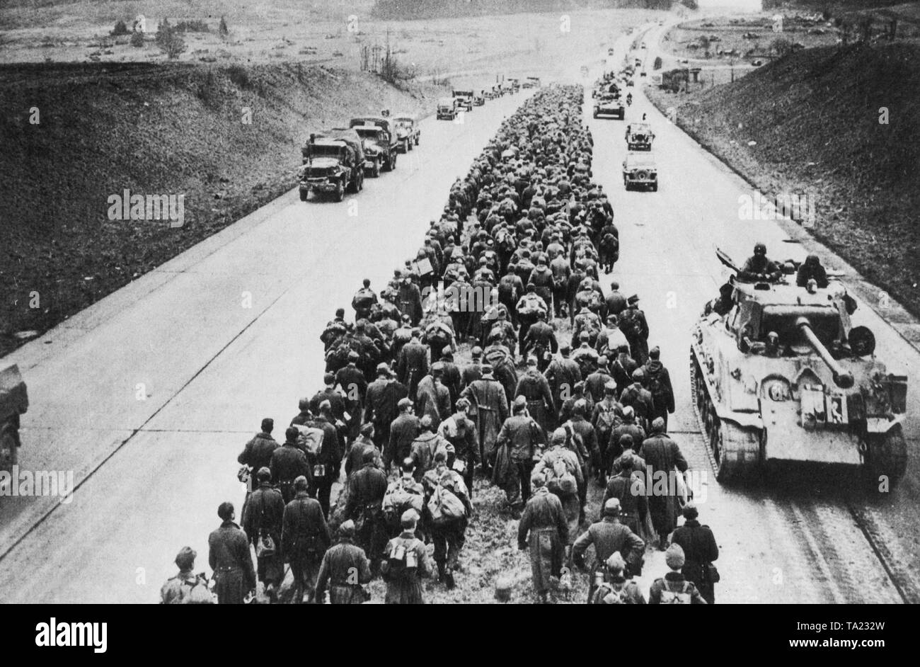 Soldiers of the German Wehrmacht pass advancing American troops in their way into war captivity. The prisoners are marching on the median strip of the motorway near the town of Giessen. Stock Photo