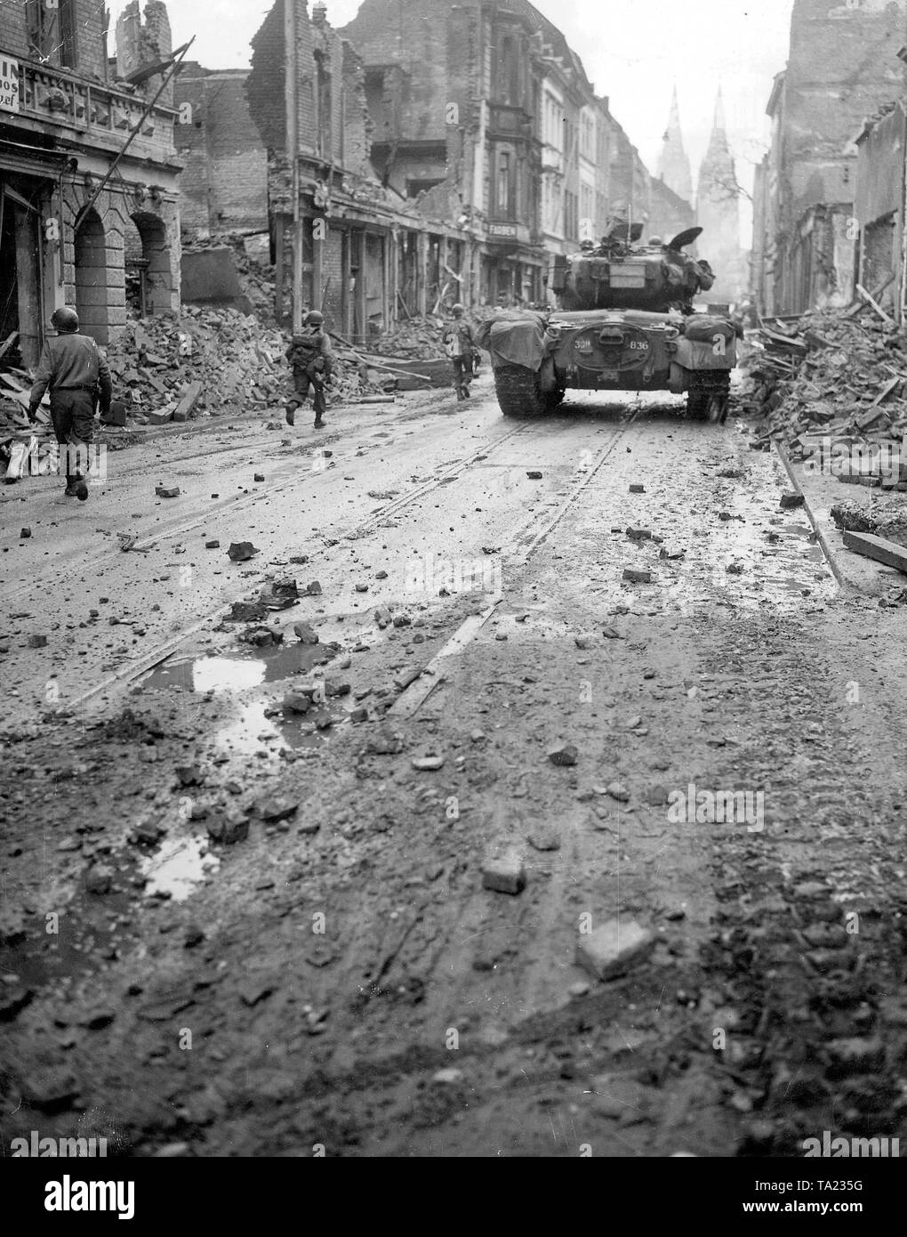 World War II: entry of American troops in Germany. The photo, taken by an American war correspondent, shows the top of the American infantry, here, protected by a heavy 'Pershing' of the 3rd Armored Division, as they fight the way through one of the heavily damaged streets of the Cologne city center towards the Cologne Dom, that is visible in the background. Stock Photo