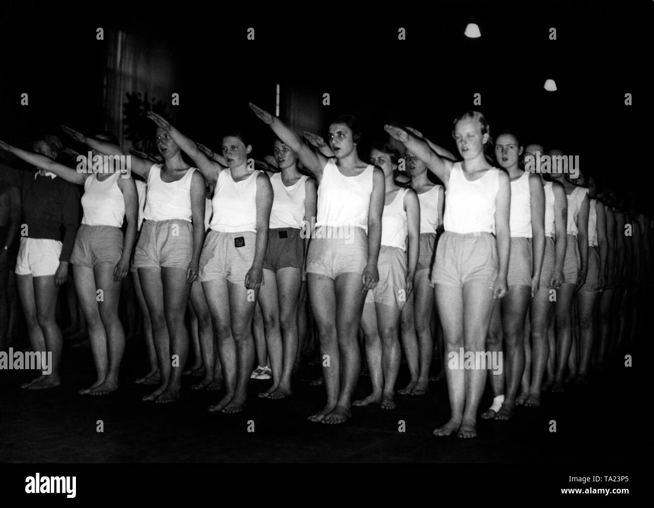 A group of female students are showing the Hitler salute on the 'Day of physical Exercises' at the gym of the Gymnastics Department of Friedrich Wilhelm University. On this occasion, Bernhard Rust gives a speech, and a sports program of gymnastics, handball, soccer and jumping/running competition takes place. Stock Photo
