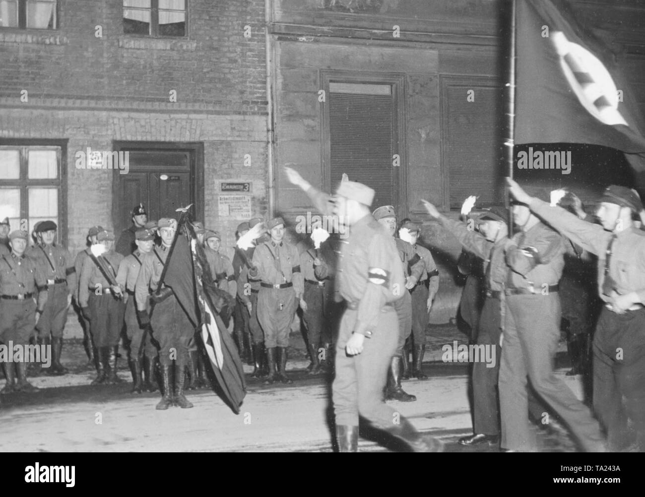 In the final phase of the Weimar Republic, SA men march through the streets of Berlin under the eyes of the police. On the wall of the house still hangs an election poster of the KPD. Stock Photo
