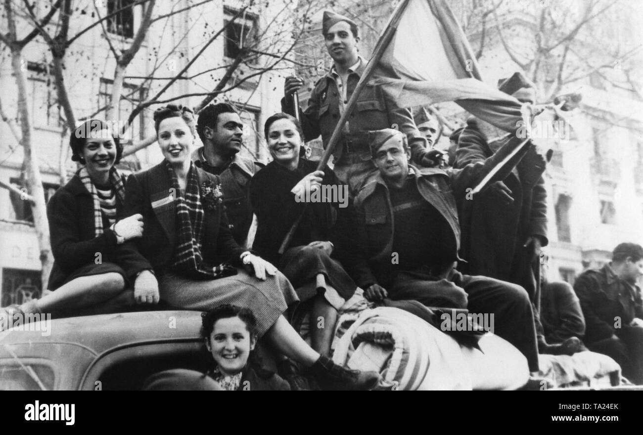 Spanish national soldiers celebrate on a truck shortly after the conquest of Barcelona by General Franco on the Rambla (promenade in the city center) with young residents of Barcelona in January, 1939. A laughing woman holds the Spanish national flag (Bandera, red-yellow-red). Stock Photo