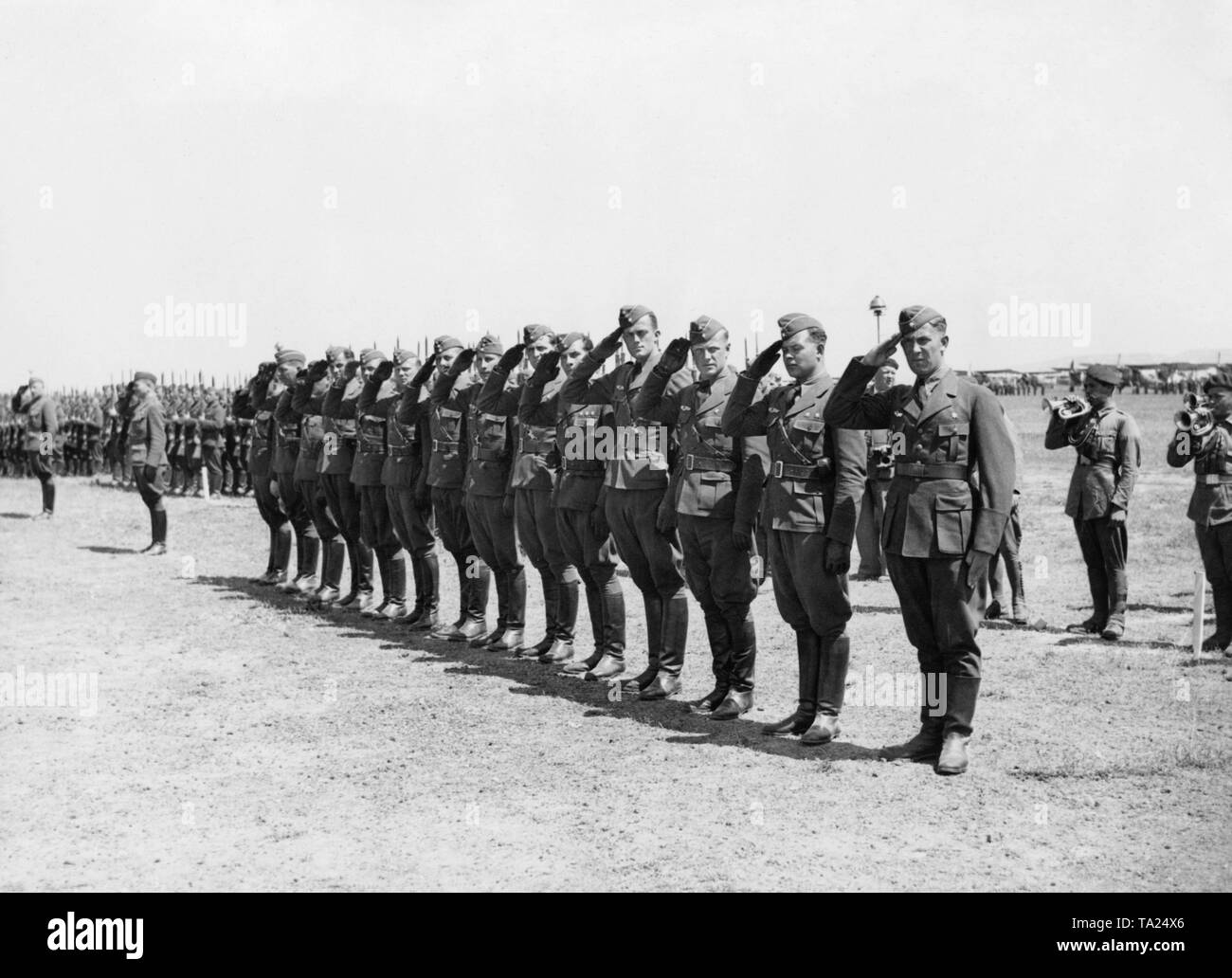 Photo of a group of German Luftwaffe (air force) officers of the Condor Legion saluting the Spanish Caudillo General Francisco Franco during a victory parade on occasion of the invasion of Madrid at Barajas airport, Madrid on March 28, 1939. Other soldiers and Spanish trumpeters have lined up as well. There are aircrafts in the background. Stock Photo